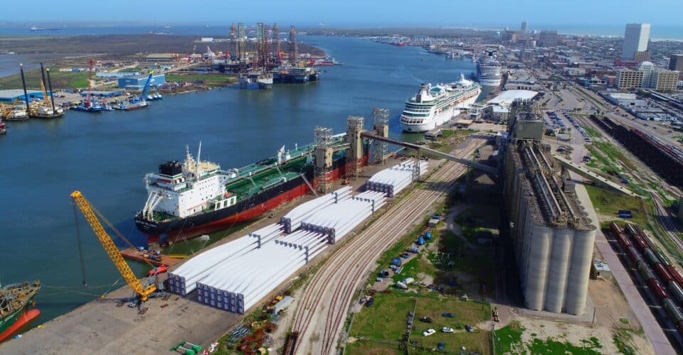 Aerial view of a construction site on the left, a body of water in the middle, and cruise ships, terminals, parking lot and streets on the right.
