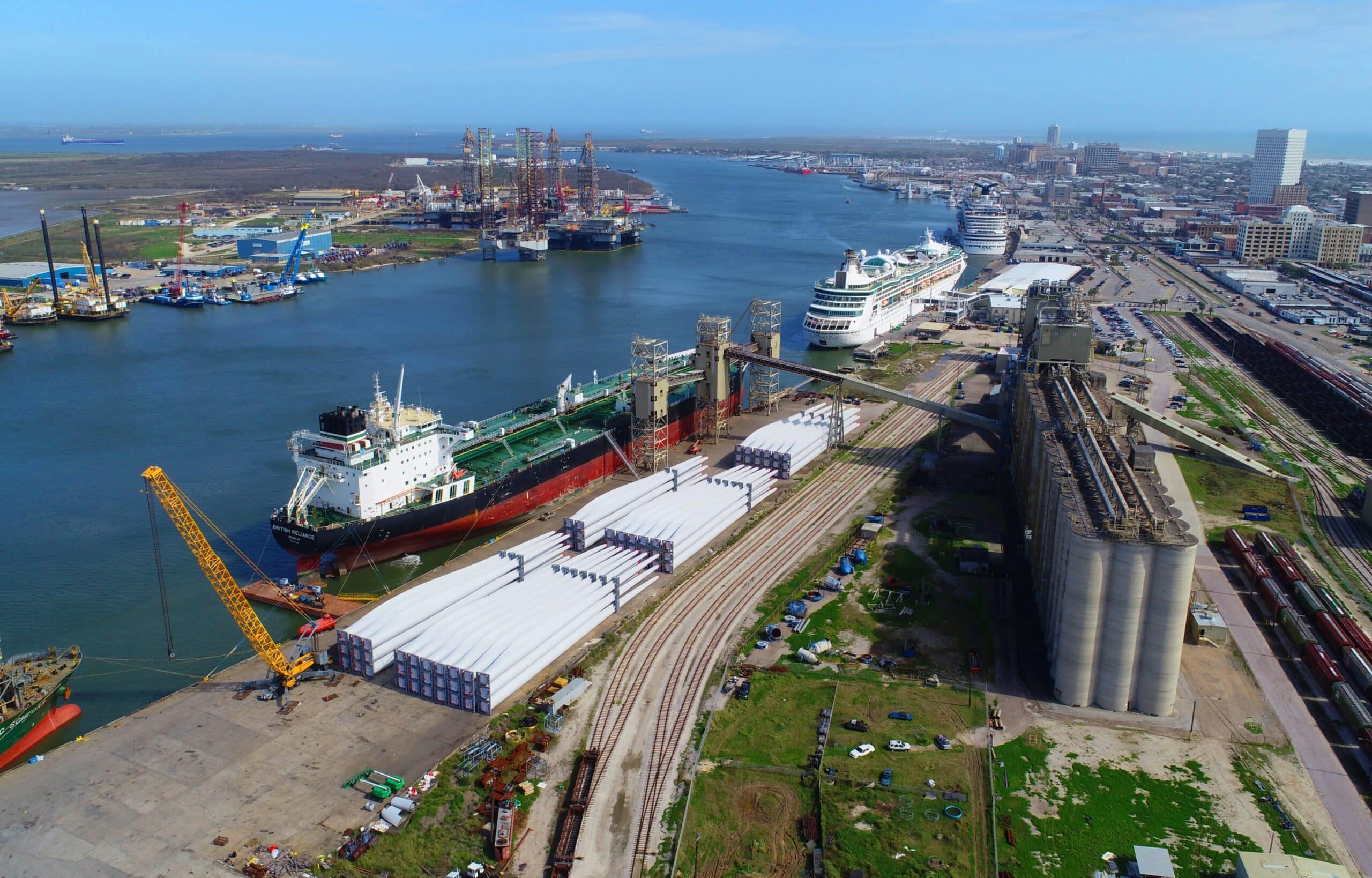 Aerial view of a construction site on the left, a body of water in the middle, and cruise ships, terminals, parking lot and streets on the right.