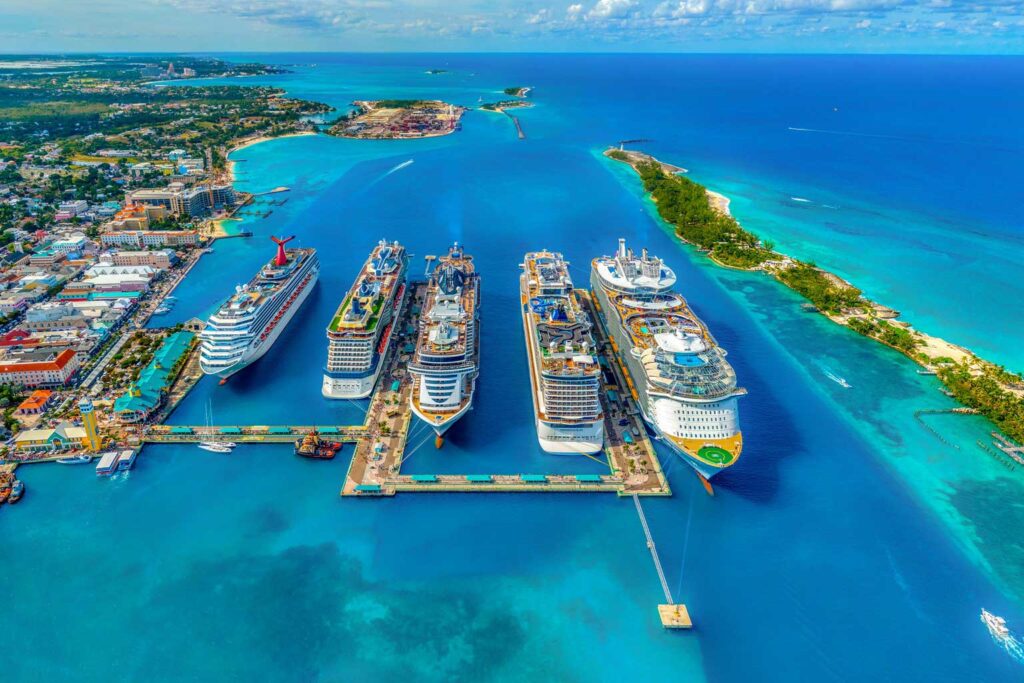 Aerial view of vibrant blue water and multiple cruise ships docked at port, highlighting cruises to the Bahamas from Galveston.